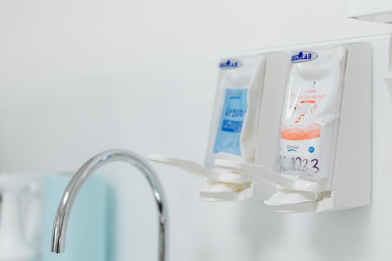 cta-bg Close-up of wall-mounted dispensers for hand sanitizers next to a hygienic sink faucet.