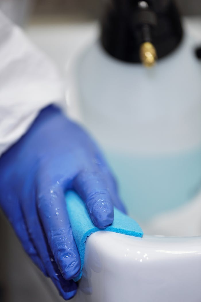home-services-02 A blue-gloved hand using a sponge to clean a white sink in a hygienic environment.